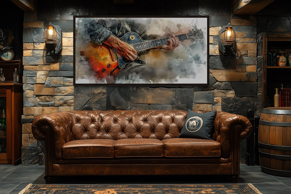 Watercolor framed canvas wall art of a hand playing a guitar, hanging above a brown leather sofa.