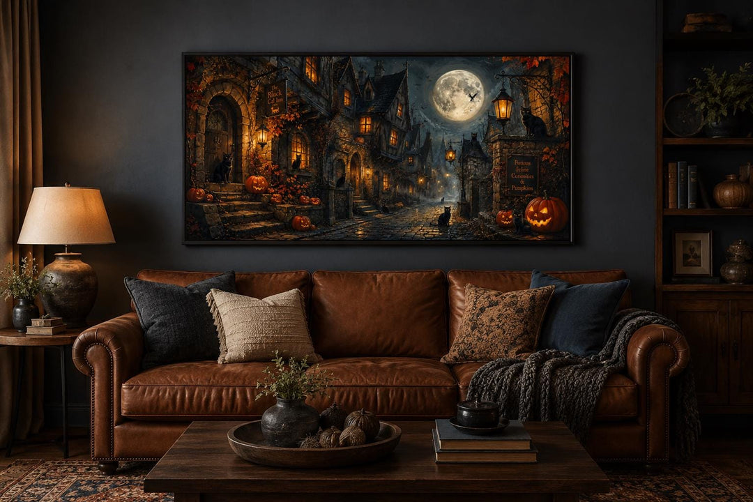 Halloween Village canvas art with black cats and pumpkins above a brown leather sofa.