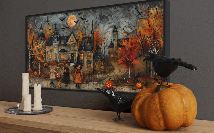 Halloween wall art of children trick-or-treating in a village, displayed on a shelf with pumpkins.