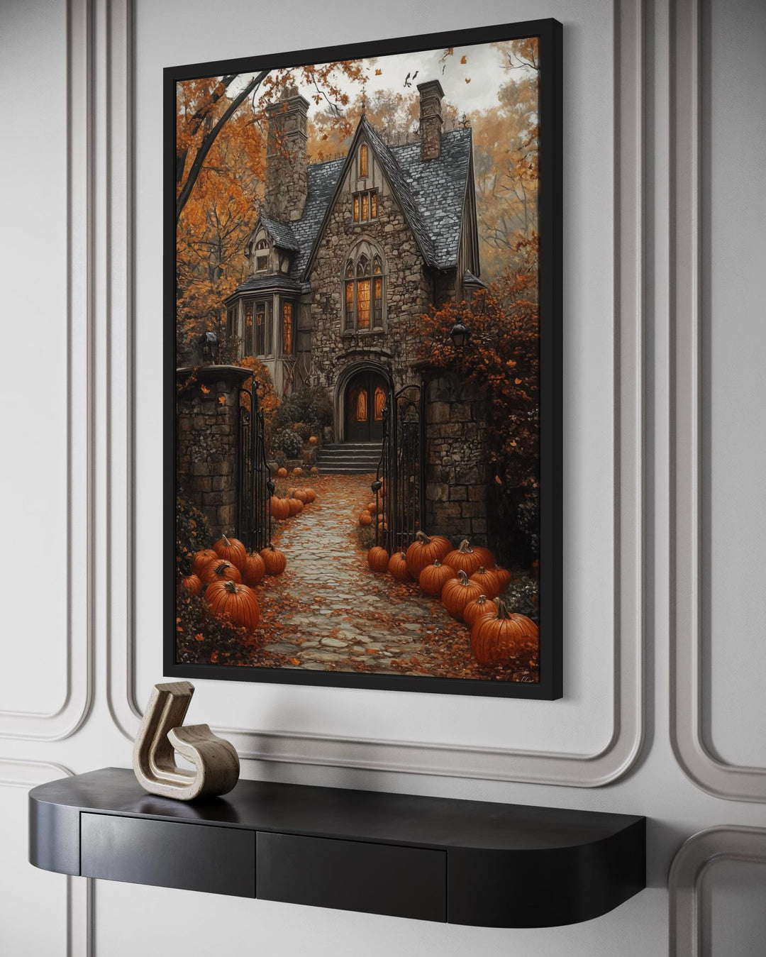 Haunted house canvas art with a pumpkin-lined path, framed and hung above a black console table.