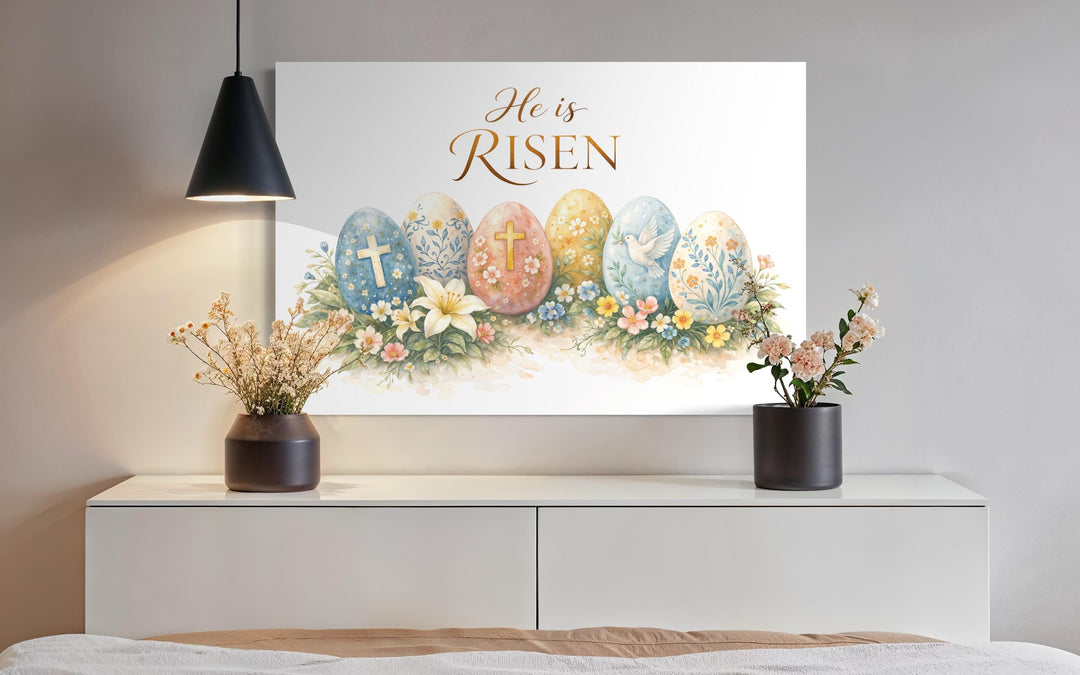 He Is Risen wall art featuring watercolor Easter eggs and florals on a canvas above a white console.