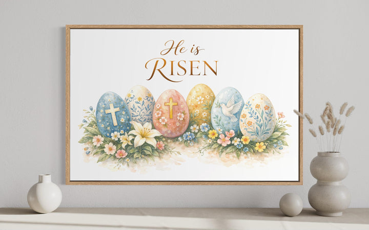 Framed watercolor wall art featuring decorated Easter eggs, flowers, and the text He is Risen.