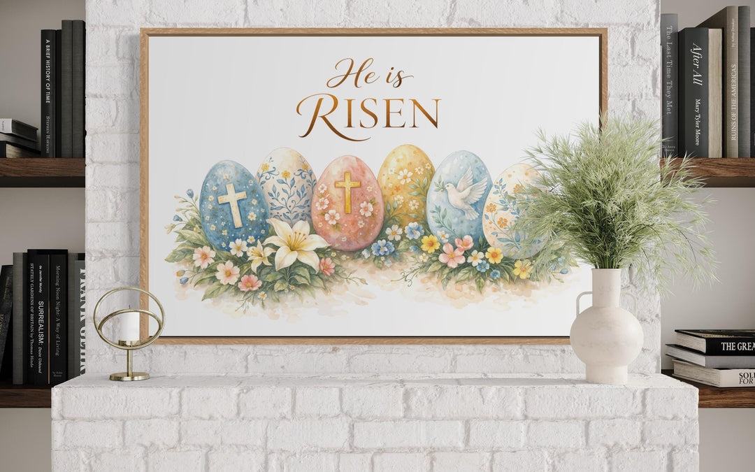 He Is Risen wall art featuring a cross and floral Easter eggs in a wooden frame on a white mantel.