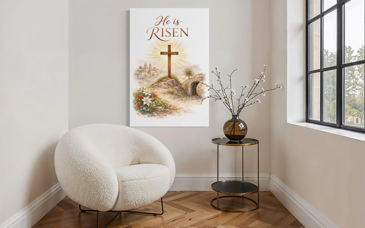 A vertical canvas print with He Is Risen text and a cross hangs in a modern, minimalist room.