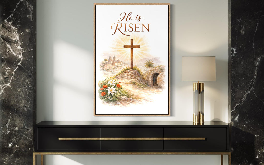 A framed He Is Risen canvas print hangs above a black console table in a modern interior.