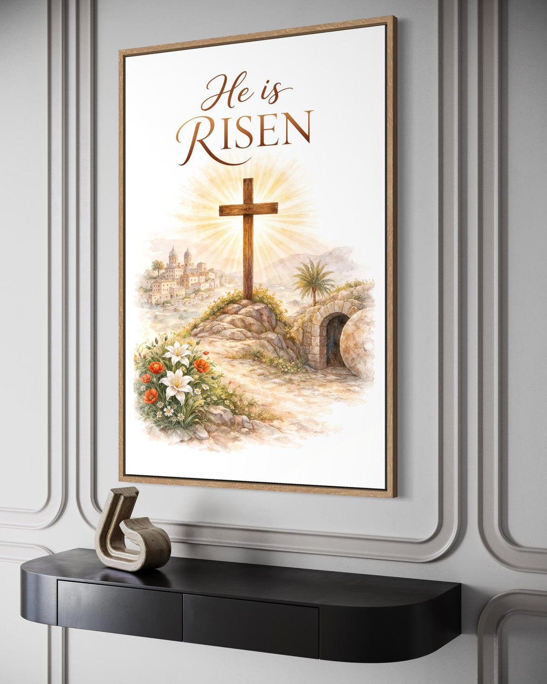 A framed watercolor canvas print of a cross and empty tomb with the text He is Risen.