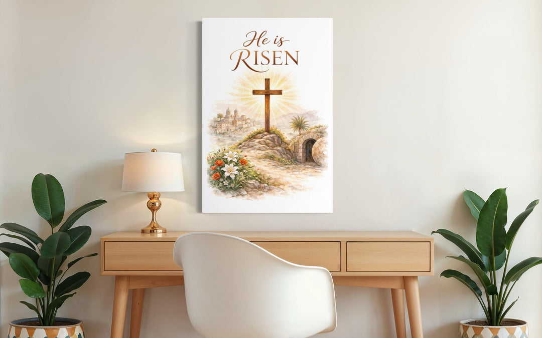 A vertical canvas print with a wooden cross and He Is Risen text hangs above a wooden desk.
