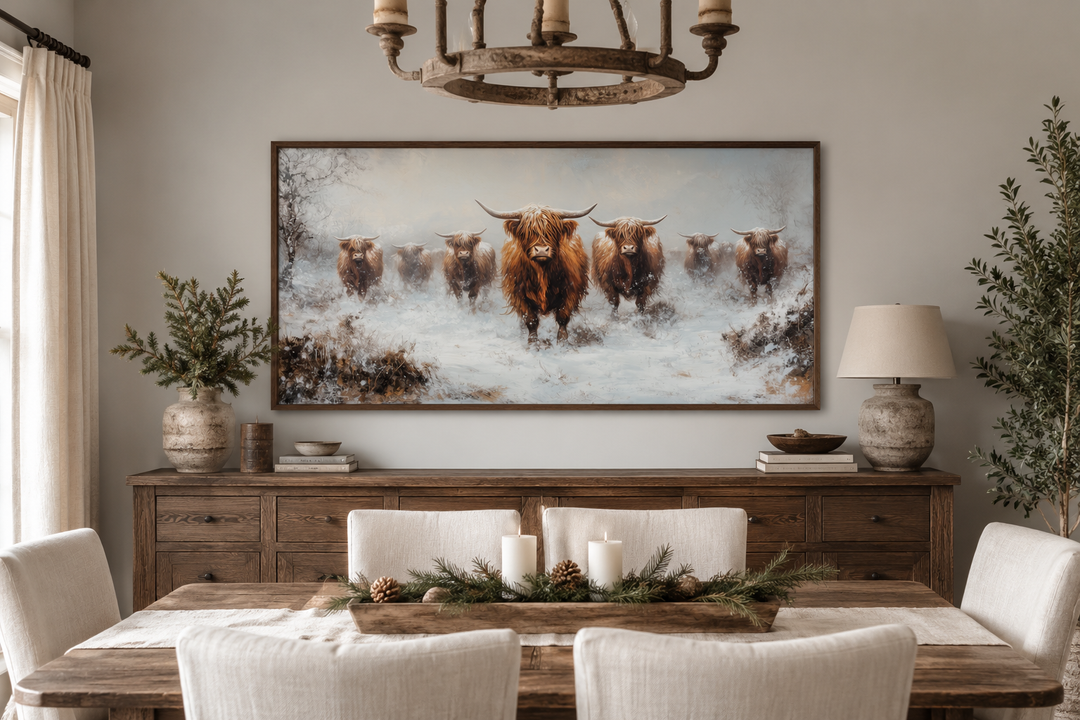 Framed canvas wall art of a herd of Highland cows in a snowy field above a wooden sideboard.