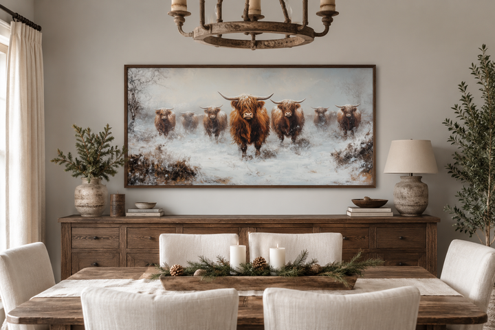 Framed canvas wall art of a herd of Highland cows in a snowy field above a wooden sideboard.