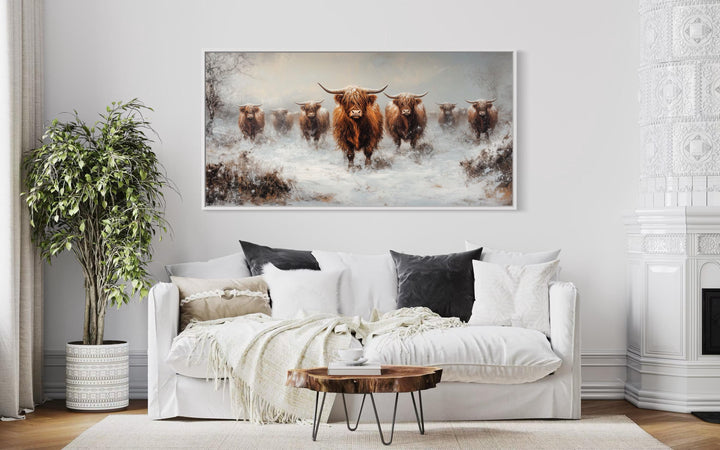A herd of Highland cows in a snowy field, framed canvas wall art above a white sofa.