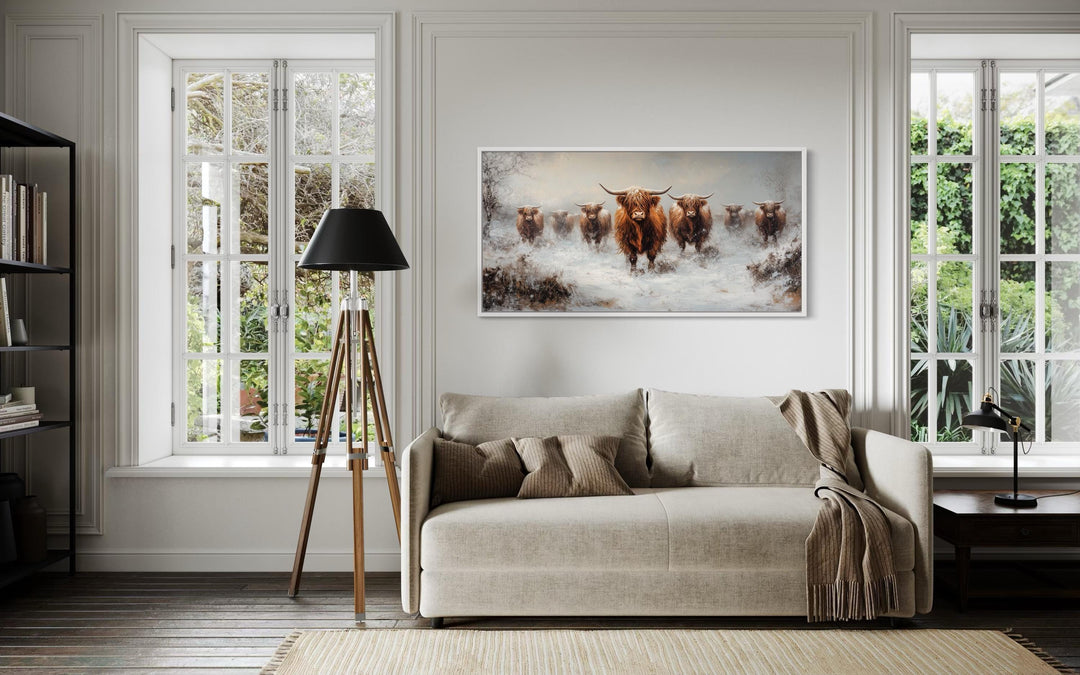 Herd of Highland cows in snow framed canvas wall art hanging above a beige sofa in a living room.