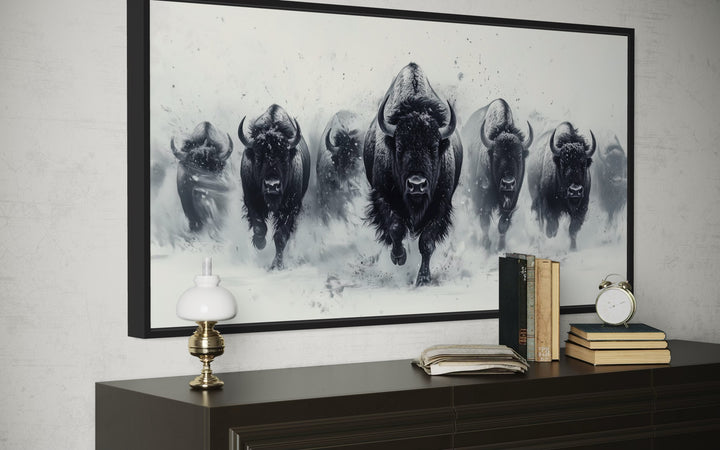 Black and white framed canvas wall art of a bison herd running through snow on a dark dresser.