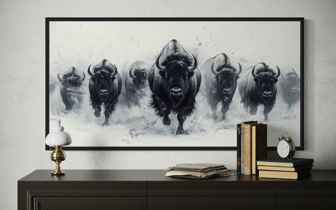 Black and white framed canvas wall art of a bison herd charging through snow on a dark dresser.