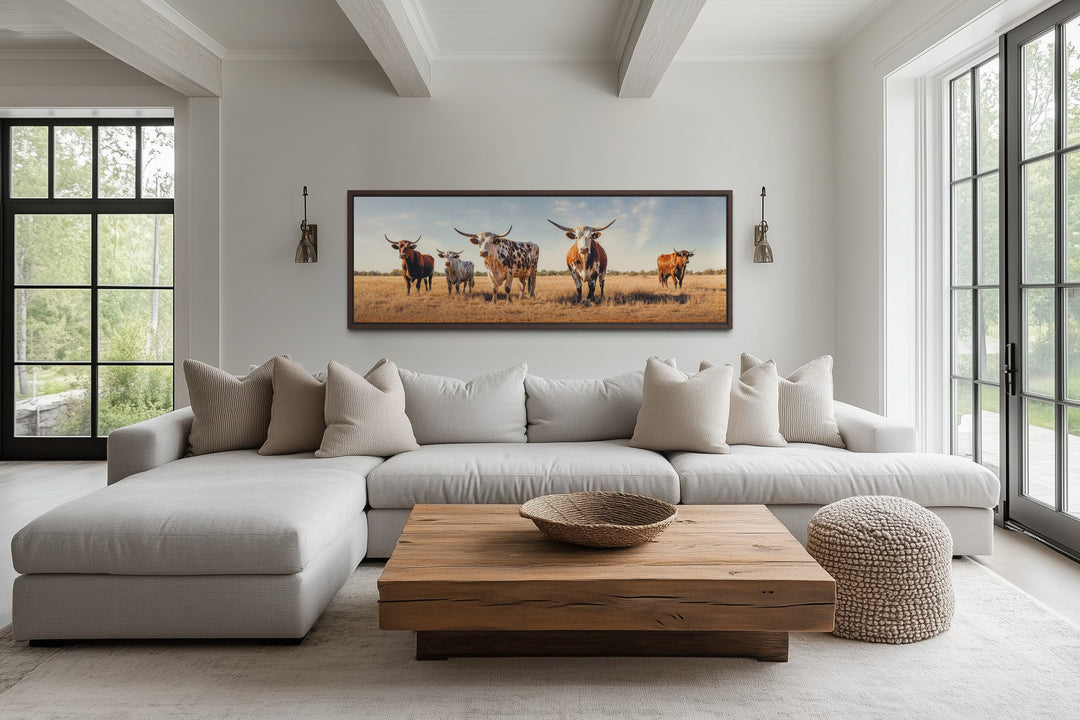 Panoramic framed canvas wall art of a herd of Texas Longhorn cows in a rustic living room.