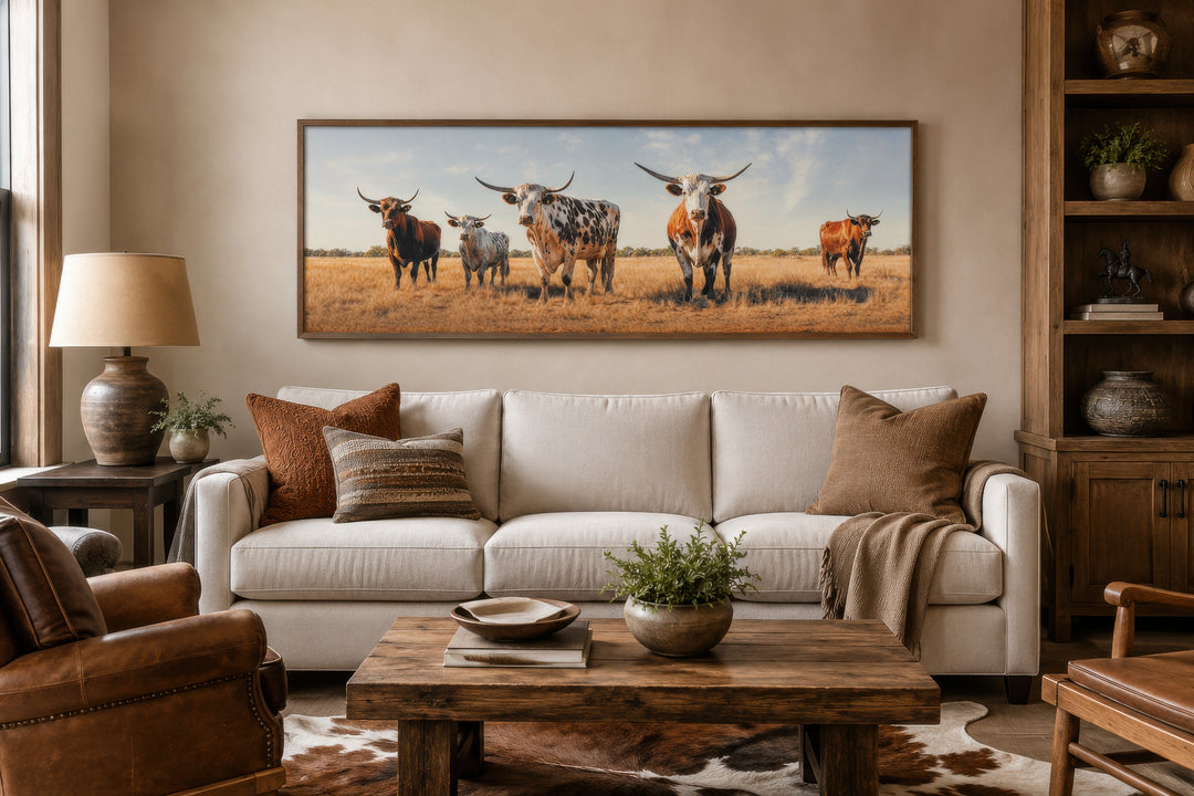 Panoramic framed canvas wall art of a Texas Longhorn cow herd above a sofa in a rustic living room.