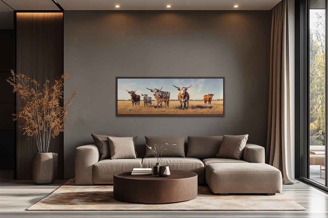 Panoramic framed canvas wall art of Texas Longhorn cows in a field above a modern sofa.