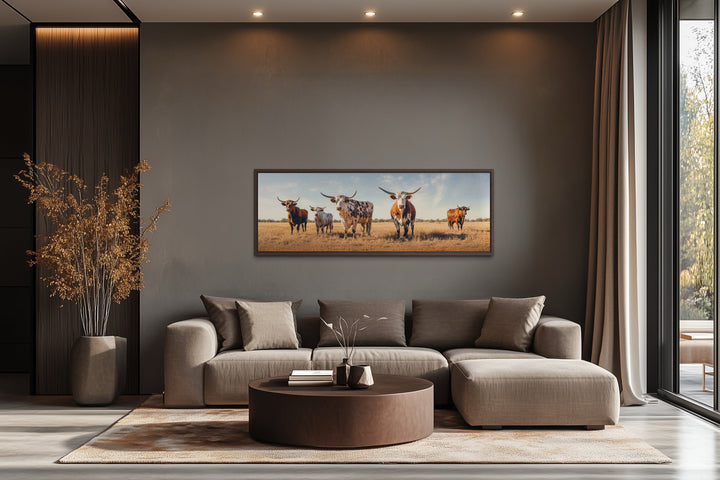 Panoramic framed canvas wall art of Texas Longhorn cows in a field above a modern sofa.