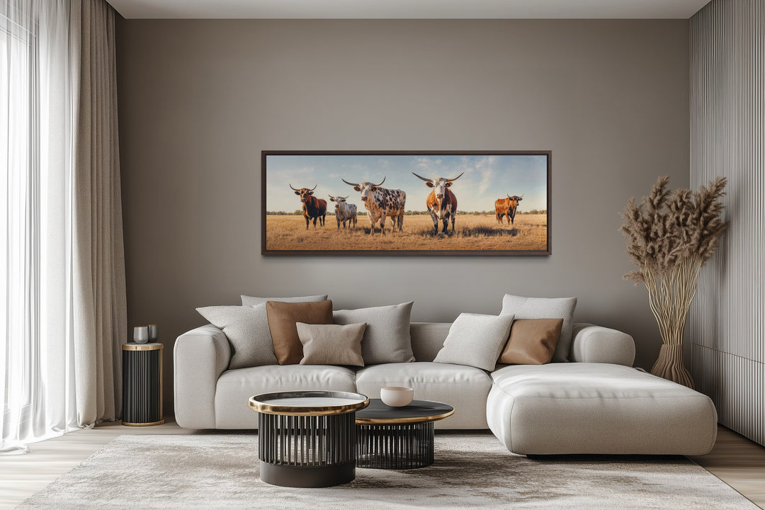 Panoramic framed canvas wall art of a Texas Longhorn cow herd in a field above a modern sofa.