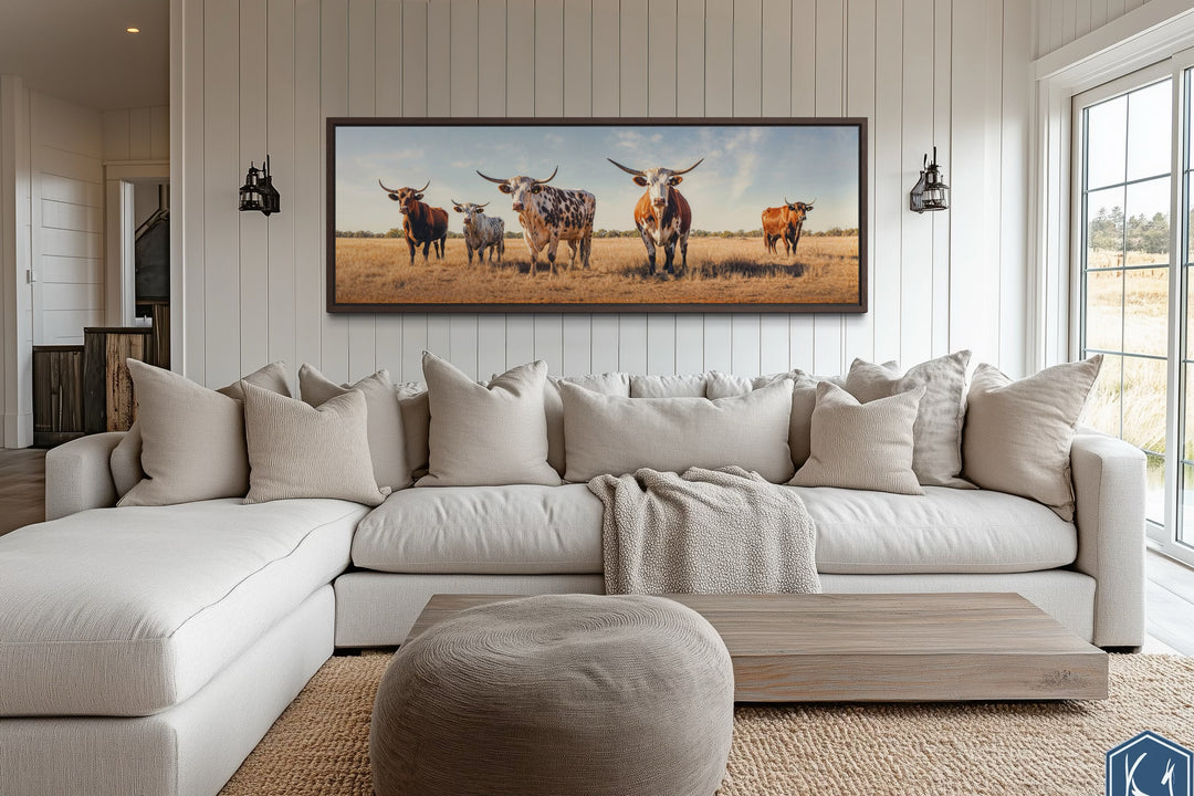 Panoramic framed canvas wall art of a Texas Longhorn cow herd above a modern sectional sofa.