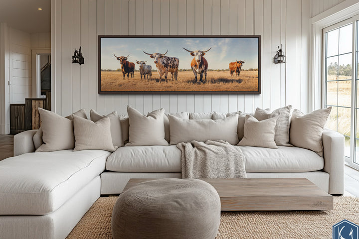 Panoramic framed canvas wall art of a Texas Longhorn cow herd above a modern sectional sofa.