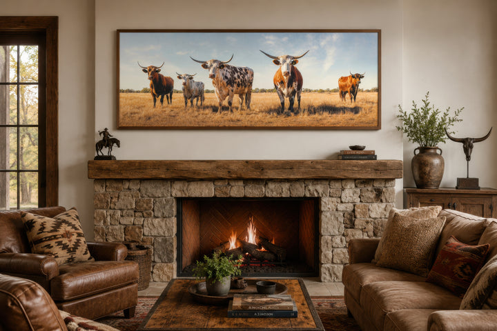 Panoramic framed canvas wall art of a Texas Longhorn cow herd above a rustic stone fireplace.