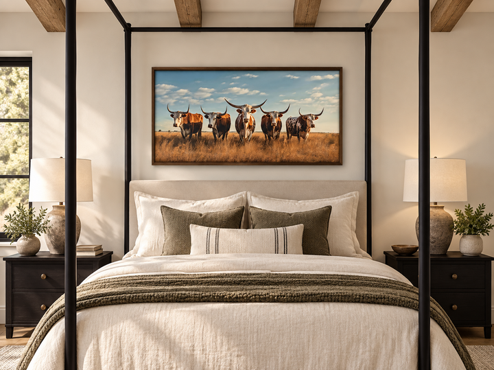 Framed canvas wall art of a Texas Longhorn herd in a field, hung above a bed in a rustic bedroom.