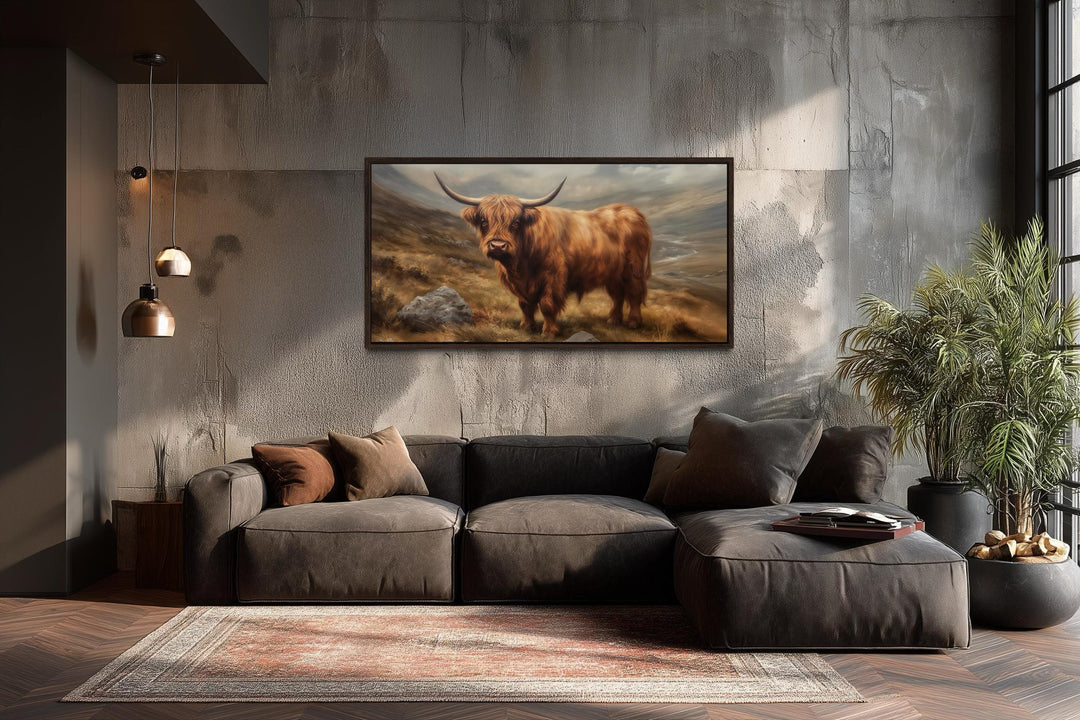 A framed canvas print of a rustic Highland cow hangs above a modern sofa in a textured room.