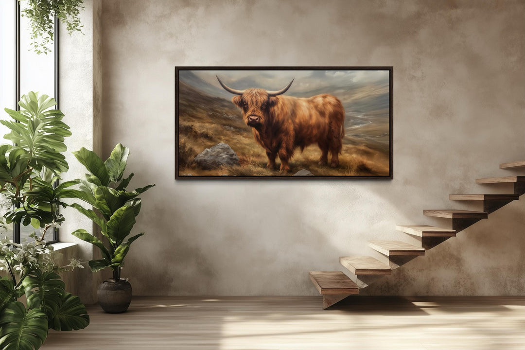 A framed canvas print of a rustic highland cow in a landscape, hung on a neutral textured wall.
