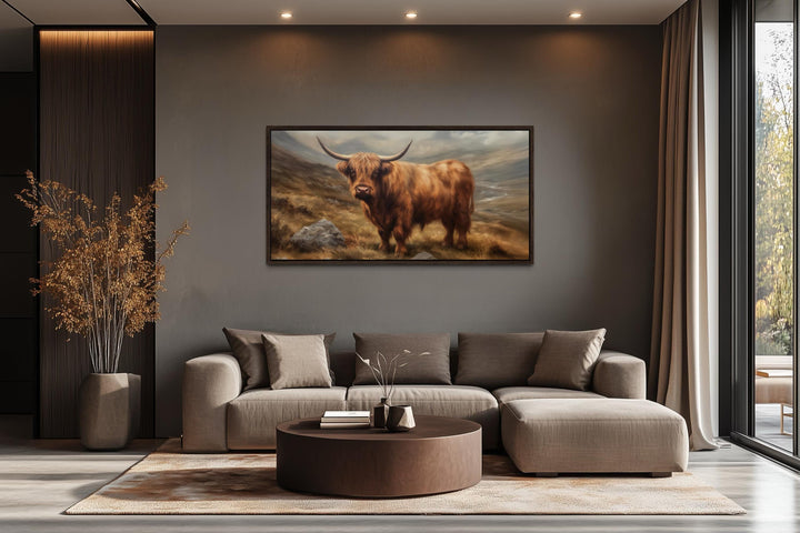 Highland cow rustic farm animal wall art in a dark wood frame above a modern brown sectional sofa.