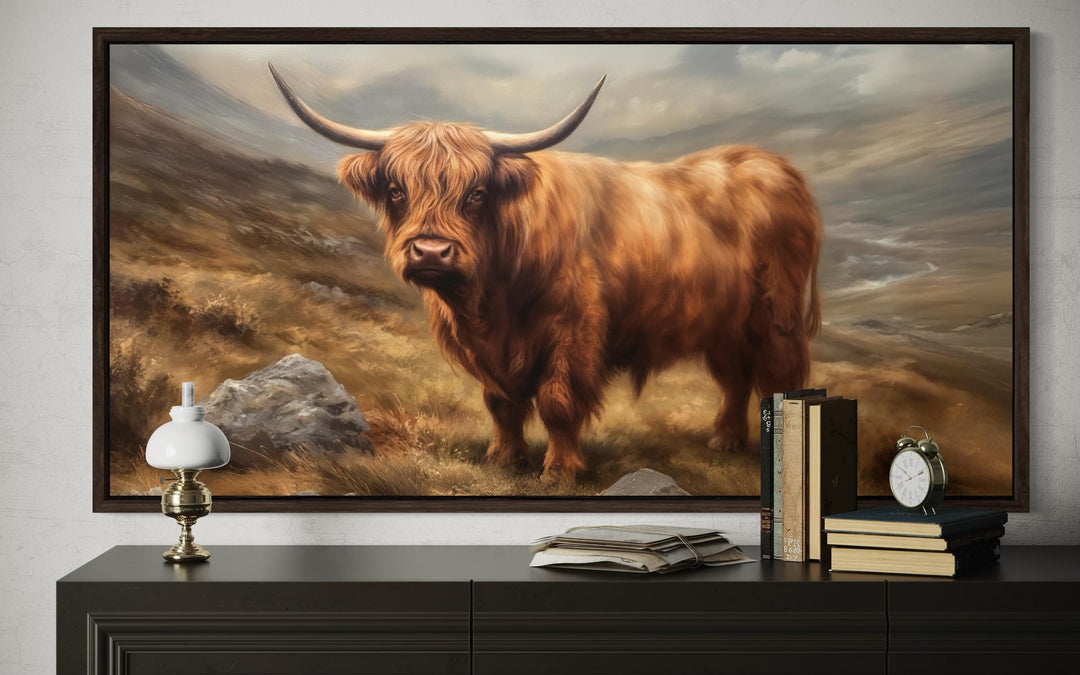 Framed canvas wall art of a rustic highland cow on a dark wood console table with vintage books.