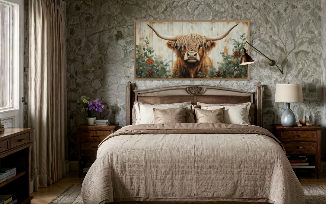 Highland cow with flowers on distressed wood framed canvas wall art above a bed in a rustic room.