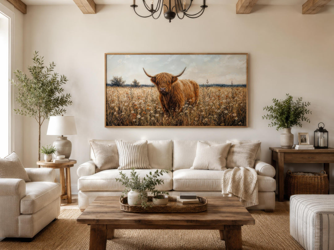 Highland Cow in Wildflower Meadow wall art in a rustic frame above a cream sofa in a farmhouse room.