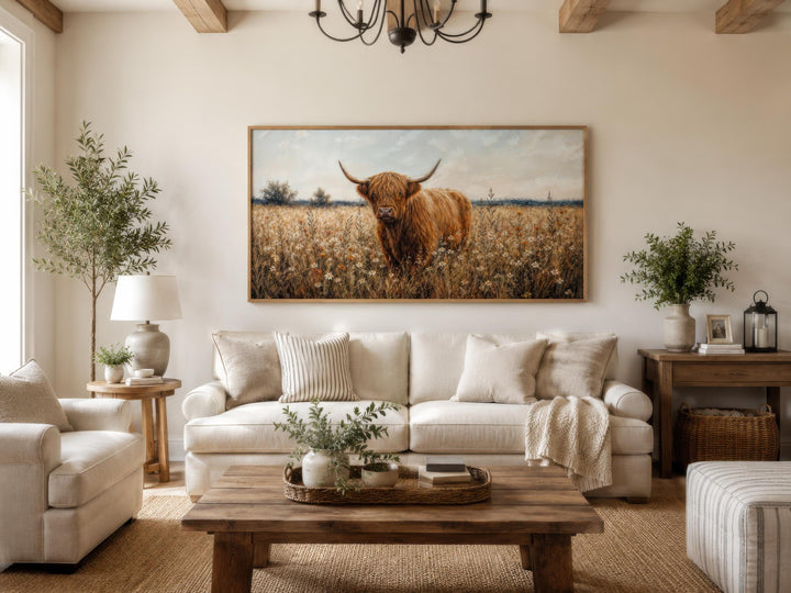 Highland Cow in Wildflower Meadow wall art in a rustic frame above a cream sofa in a farmhouse room.