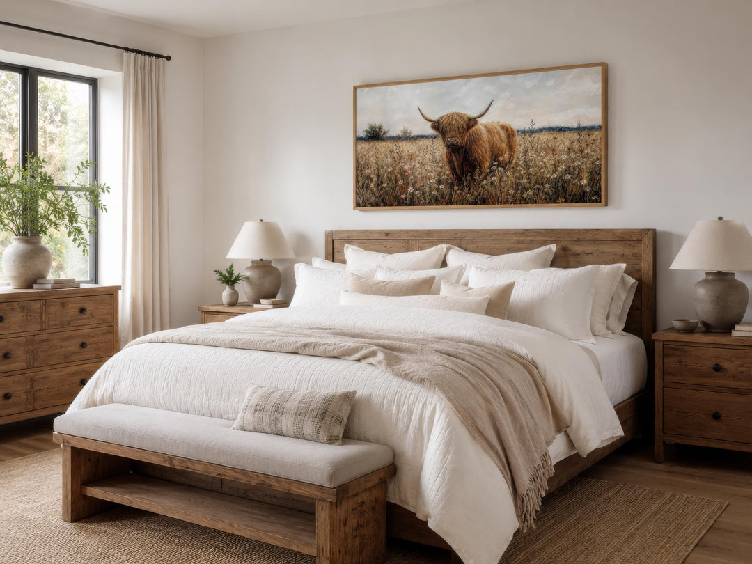 Highland cow in a wildflower meadow canvas print hanging above a rustic wooden bed frame.