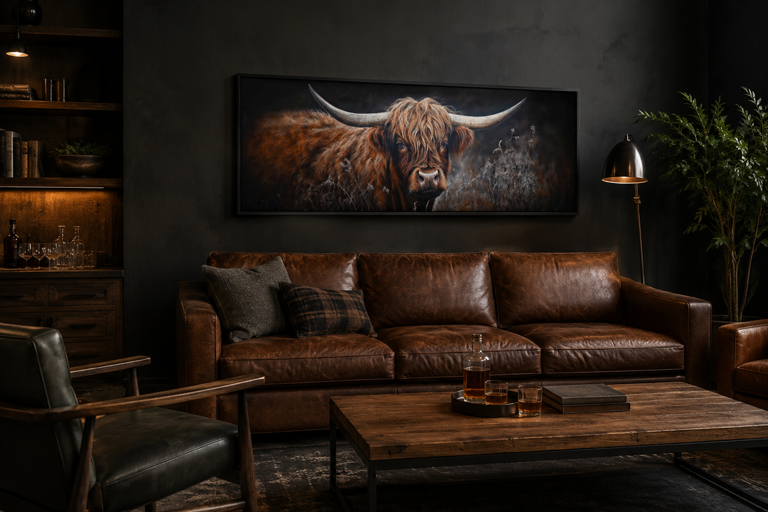 Long horizontal canvas wall art of a dark Highland cow above a brown leather couch in a dark room.