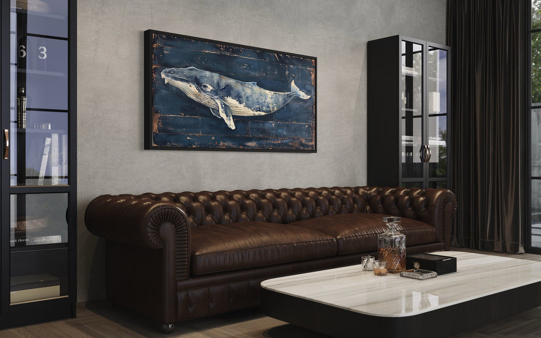 Humpback whale wall art on navy blue distressed wood canvas above a brown leather chesterfield sofa.