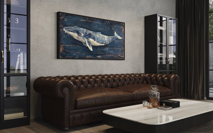 Humpback whale wall art on navy blue distressed wood canvas above a brown leather chesterfield sofa.