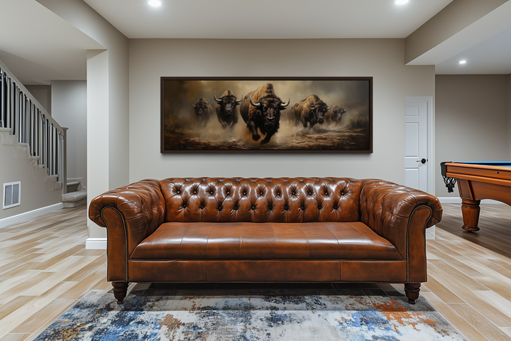 A long horizontal framed canvas featuring a herd of running bison hangs above a leather sofa.