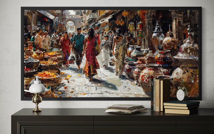 Framed Indian market painting on a dark sideboard with books, a lamp, and a clock.