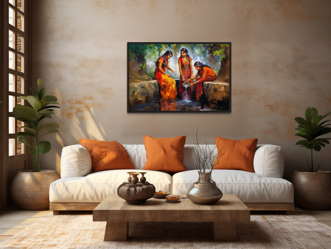 Framed canvas wall art of Indian women in vibrant saris at a well, styled in a warm living room.