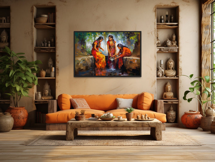 Framed canvas wall art of Indian women in saris at a well, hanging above an orange sofa.