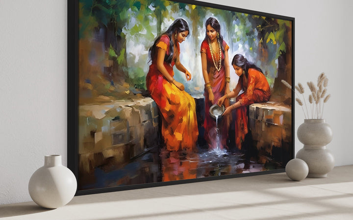 Framed canvas wall art of three Indian women in vibrant saris gathering water at a well.