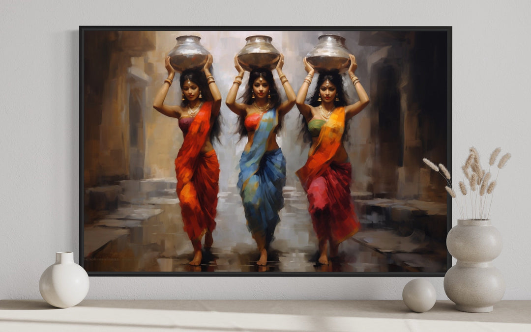 Framed canvas wall art of three Indian women in vibrant saris carrying water pots on their heads.