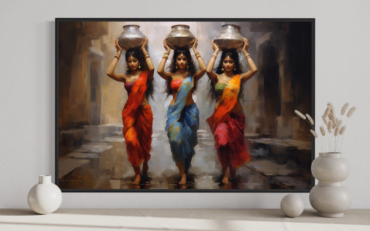 Framed canvas wall art of three Indian women in vibrant saris carrying water pots on their heads.