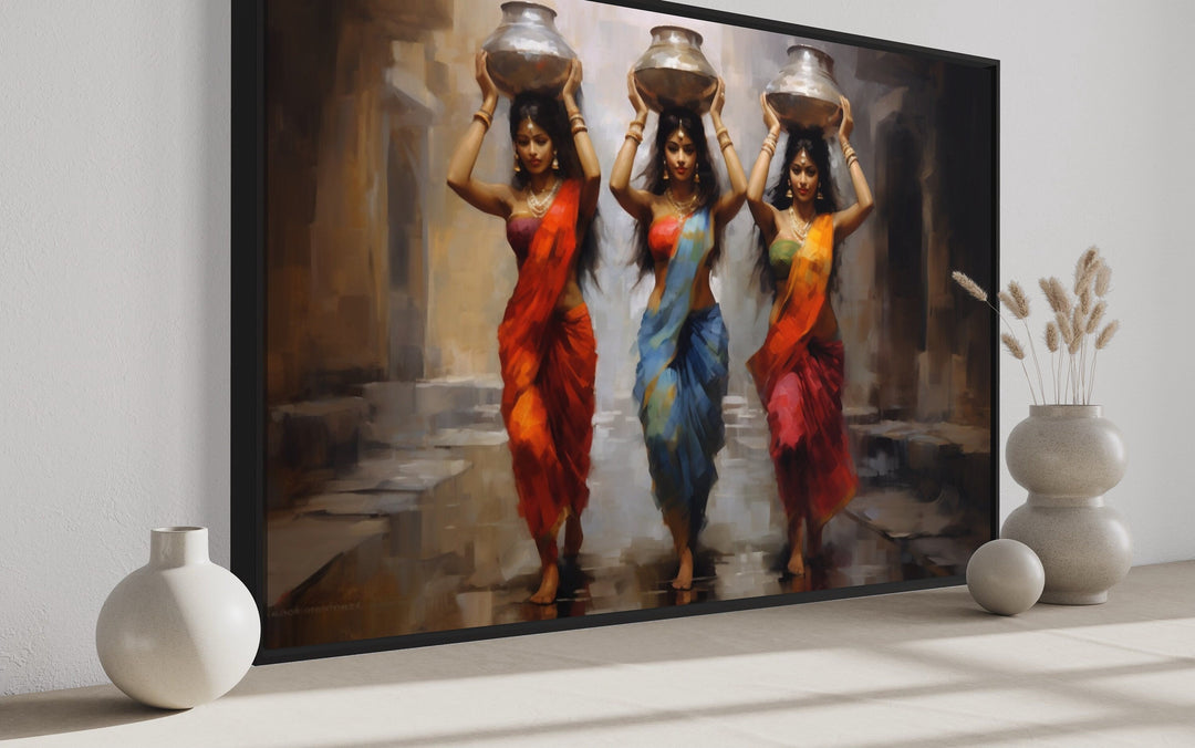 Framed canvas wall art of three Indian women in vibrant saris carrying water pots on their heads.