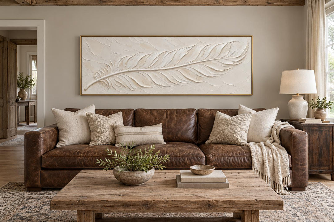 Long narrow canvas wall art featuring a cream plaster-effect feather above a brown leather sofa.