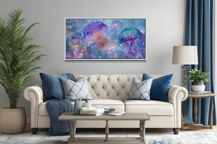 A horizontal canvas print of colorful purple and blue jellyfish hangs above a neutral tufted sofa.