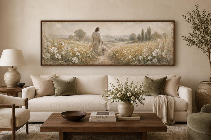 Wide horizontal canvas art of Jesus and a lamb in a wildflower field above a modern cream sofa.
