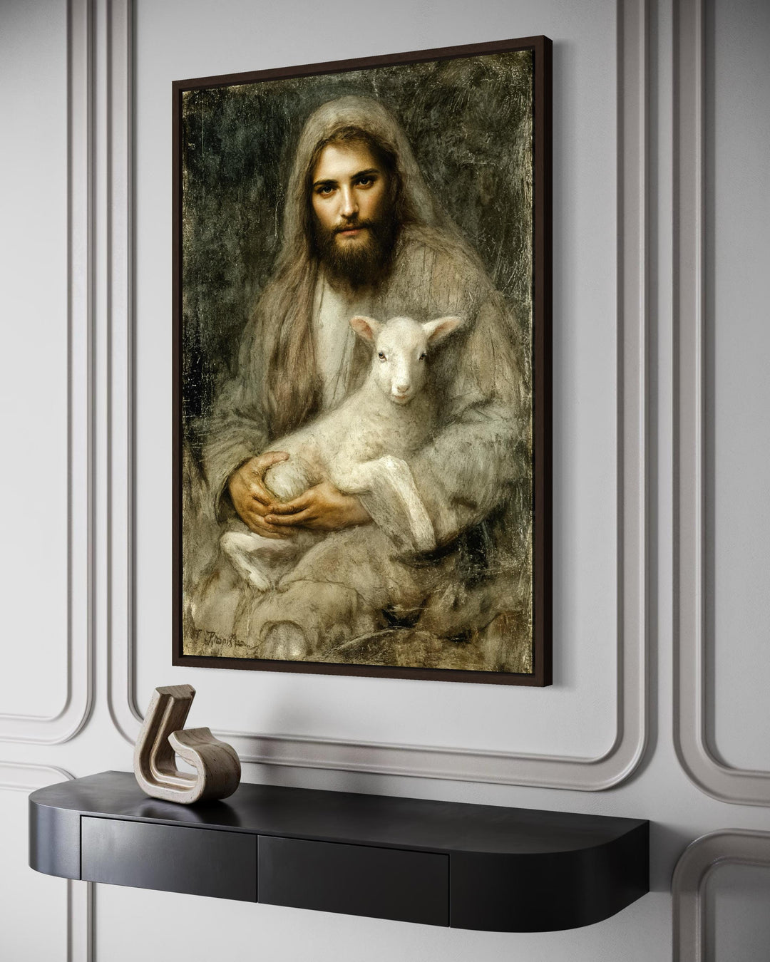 A framed canvas painting of Jesus holding a lamb, displayed on a wall above a black console table.