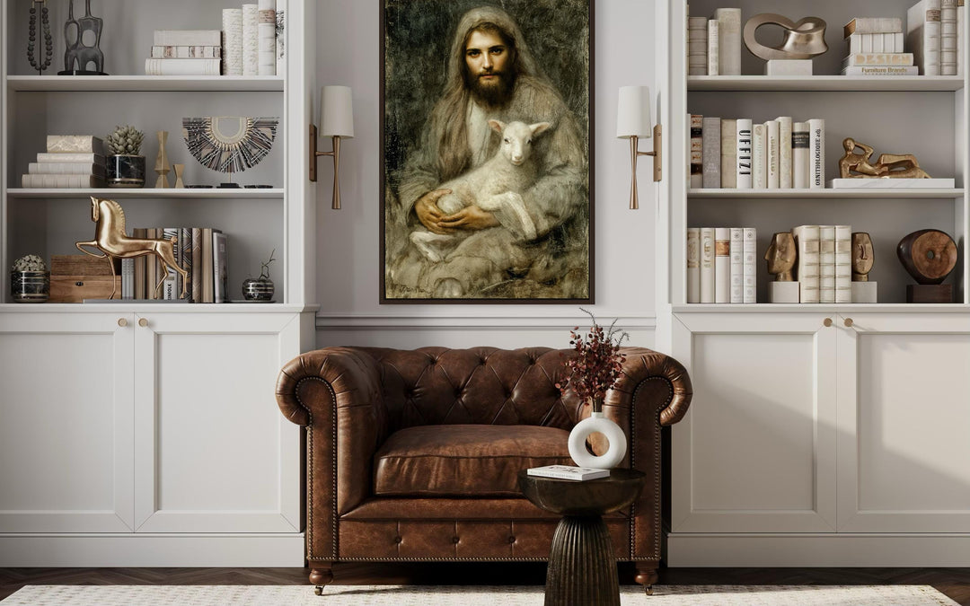 Framed canvas wall art of Jesus holding a lamb, displayed above a brown leather armchair.
